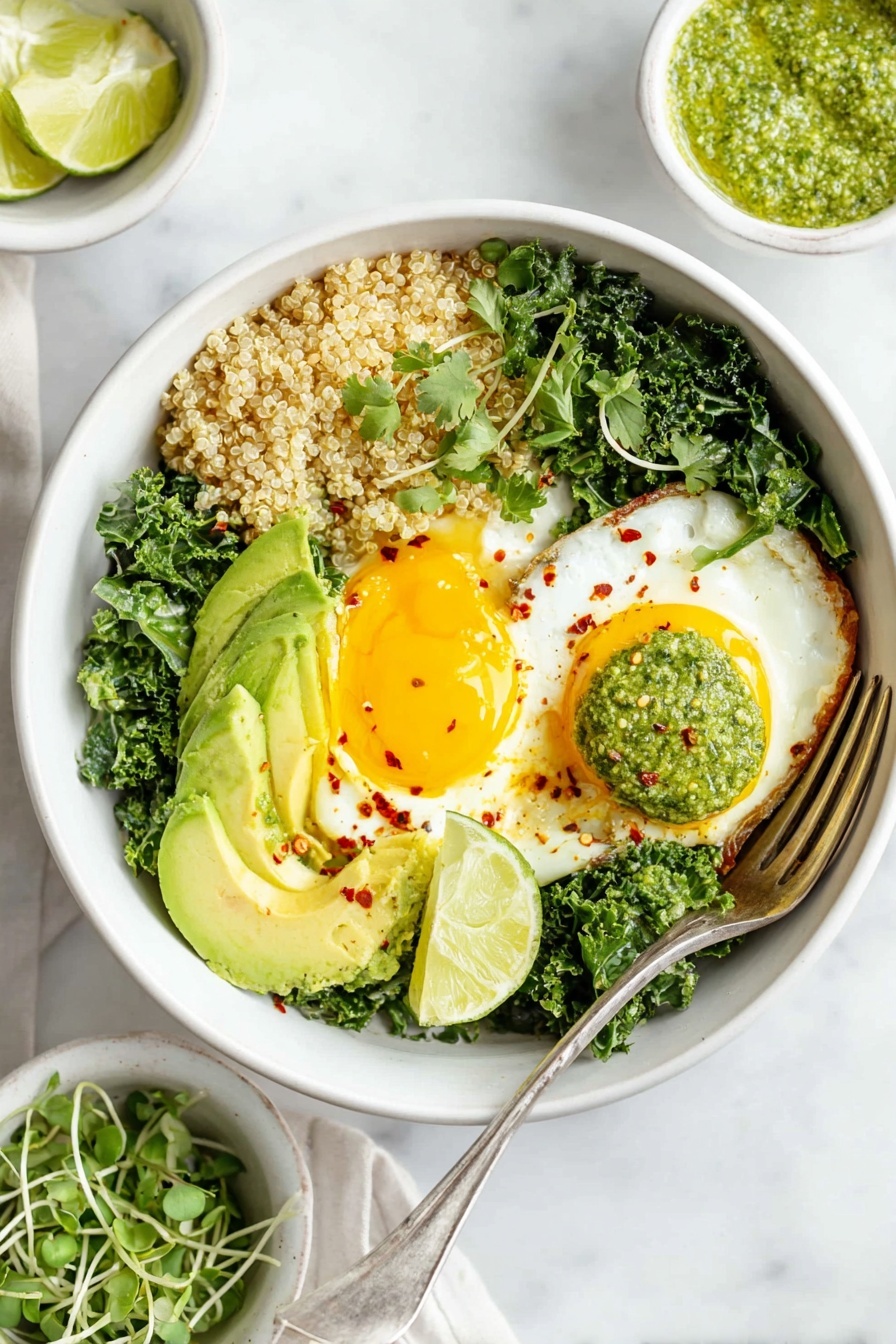 A white bowl sits on a white marbled surface, filled with four main layers: fluffy tan quinoa on the left, green kale leaves cooked and spread on the right and bottom, two sunny yellow fried eggs with bright yolks placed over the quinoa, and sliced avocado fanned out over the kale. A dollop of light green pesto sauce sits near the center, topped with small red chili flakes. Two lime wedges rest on the kale near the avocado, and a fork is placed inside the bowl on the left side. Nearby are small white bowls containing green pesto and fresh microgreens. Photo taken with an iphone --ar 2:3 --v 7