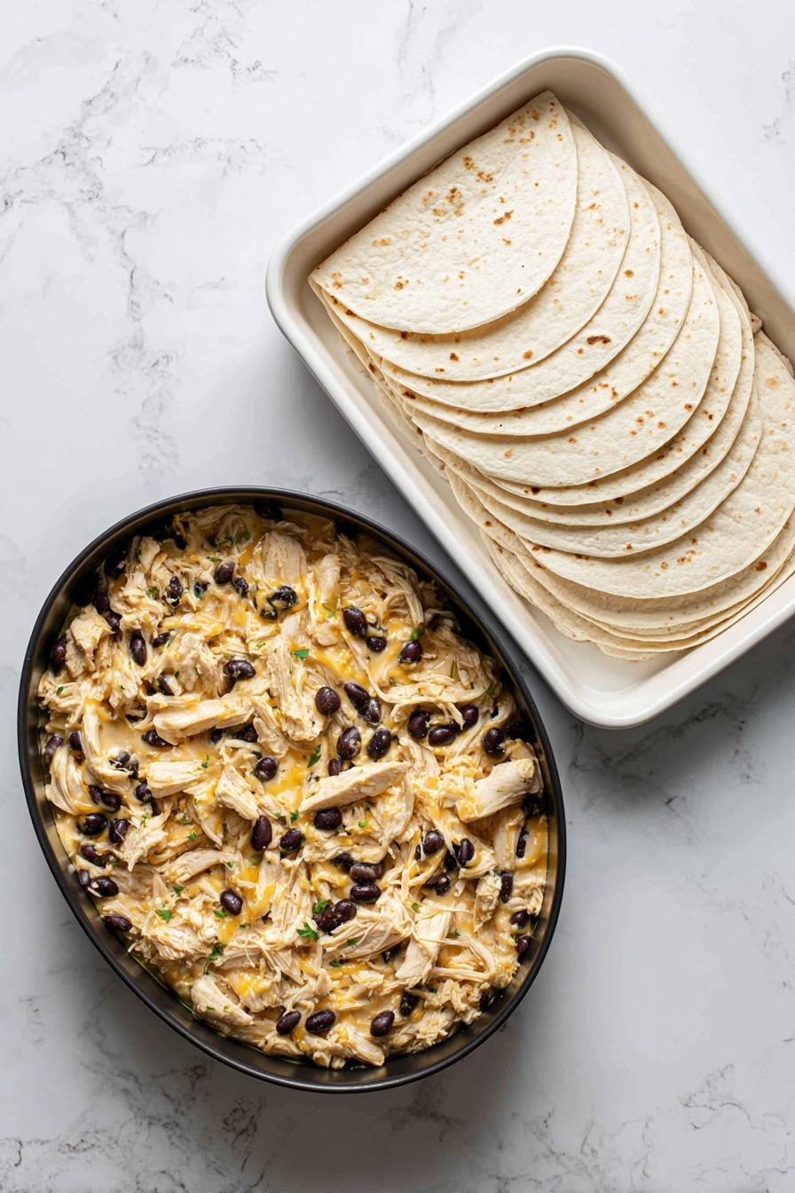 The dish shows a stack of two layered enchiladas placed on a round white plate with a light brown rim, set on a white marbled surface. The enchiladas are covered with melted yellow cheese, black beans, small diced red tomatoes, green peppers, and bits of cilantro, giving a colorful and textured look on top. To the left of the enchiladas are several triangular, golden-yellow tortilla chips arranged in a small pile. A dollop of smooth white sour cream rests beside the chips near the edge of the plate. Fresh cilantro leaves and a white cloth are slightly visible in the blurred background. Photo taken with an iphone --ar 2:3 --v 7