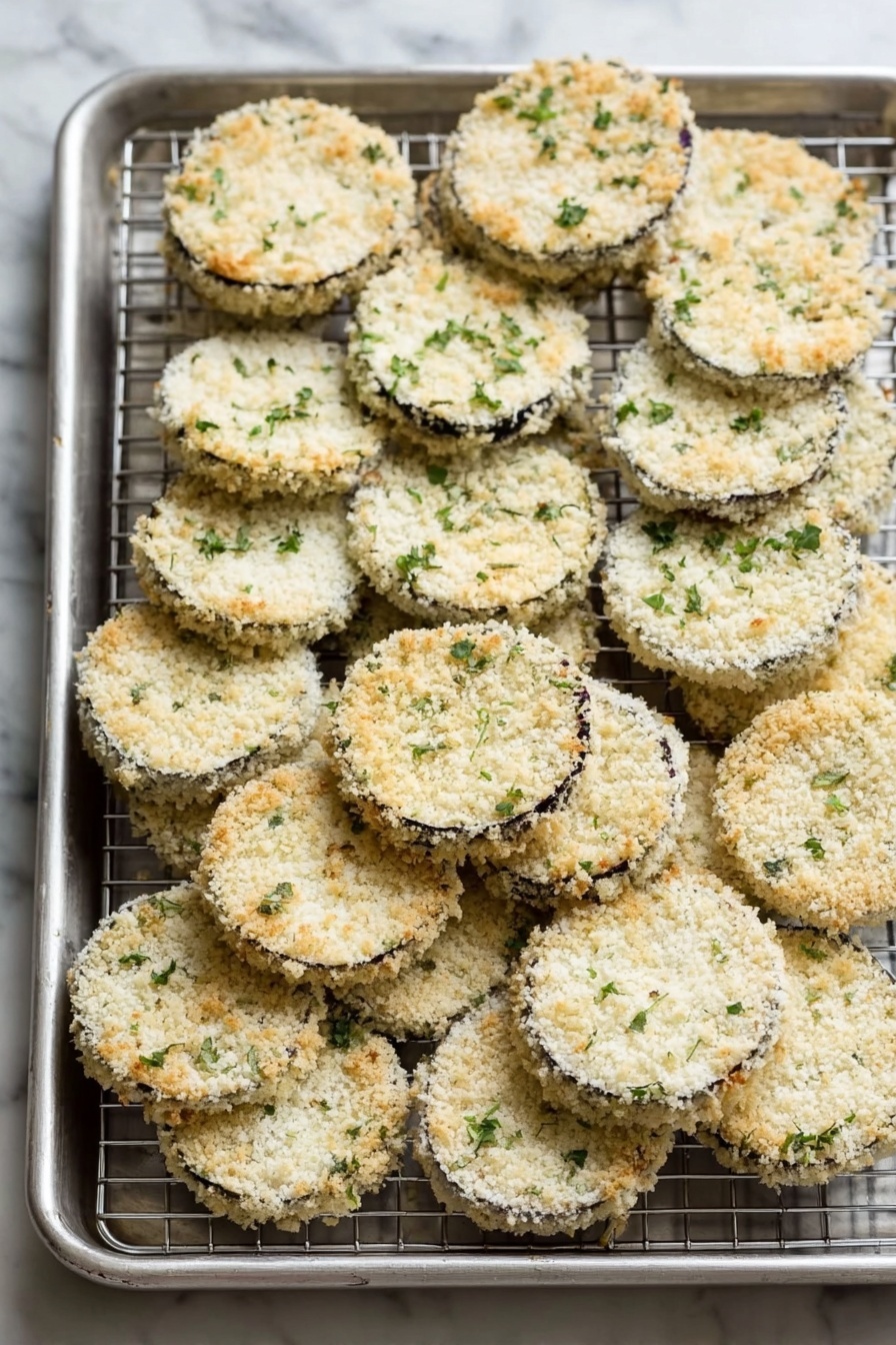 A white plate holds five pieces of round fried eggplant arranged in a small pile, each layer showing a golden brown crispy texture along the edges. On top of each eggplant is a layer of bright red tomato sauce with a smooth texture, followed by a thick, melted white mozzarella cheese layer that is slightly browned in spots and sprinkled lightly with green herbs. Two fresh green basil leaves are placed at the top right edge of the plate. The plate sits on a white marbled surface with soft natural light highlighting the glossy cheese. photo taken with an iphone --ar 2:3 --v 7