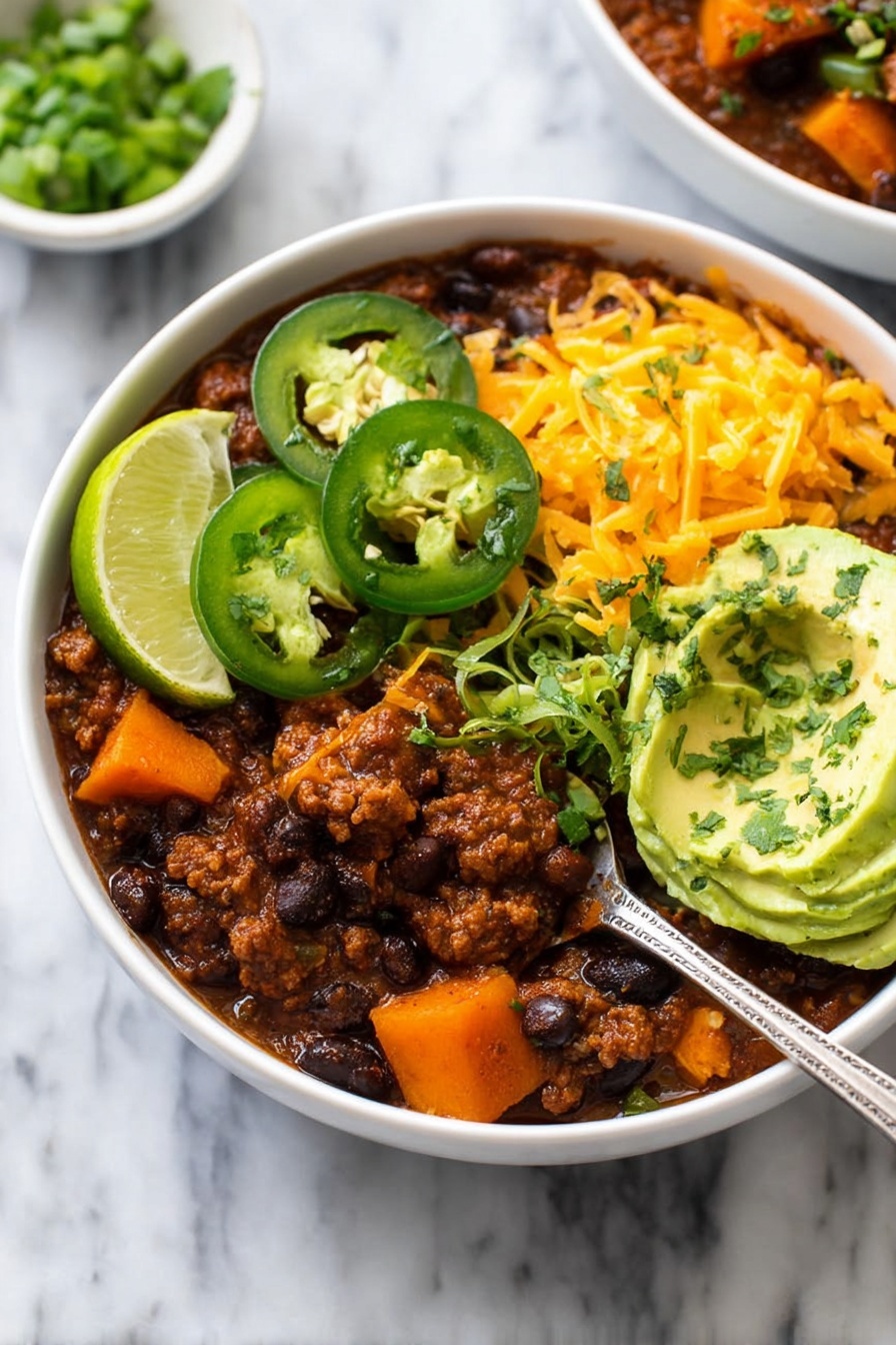 A white bowl filled with three layers: the bottom layer is a thick brown chili with visible black beans, chunks of orange sweet potato, and small pieces of ground meat, topped with bright orange shredded cheese scattered on one side; the middle layer has two green jalapeño slices and a large scoop of smooth light green avocado slices sprinkled with chopped dark green herbs, and a wedge of bright yellow-green lime placed near the edge; the top layer includes fresh chopped green onions spread gently over the dish. A silver spoon scoops some chili from the bowl, and the background is a white marbled surface. Photo taken with an iphone --ar 2:3 --v 7