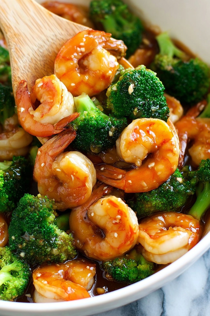 A close-up of a white bowl filled with cooked shrimp and bright green broccoli florets, all coated in a glossy brown sauce with small bits of garlic visible. The shrimp are orange with white flesh, curled and shiny, mixed evenly with the broccoli. A light-colored wooden spatula is stirring the ingredients, lifting some shrimp on top. The background shows a white marbled texture. photo taken with an iphone --ar 2:3 --v 7